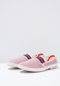Scarpe slip-on rosse e bianche con una fantasia, strisce blu, tomaia in tessuto, superficie testurizzata e suola in gomma bianca con dettagli di cucitura.