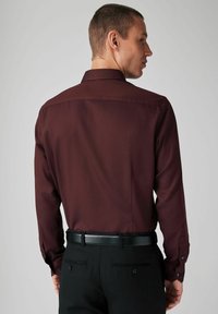Burgunderfarbendes Langarmhemd mit glatter Textur, einem Button-Down-Kragen und schwarzen Knöpfen; kombiniert mit schwarzen Hosen und einem schwarzen Gürtel.