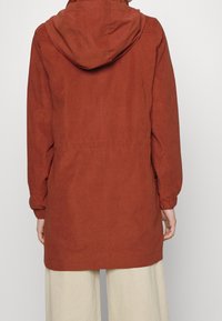 Chaqueta roja con capucha, de corte relajado, puños elásticos y cintura ajustable con cordón. Hecha de tejido texturizado, presenta un diseño simple y limpio.