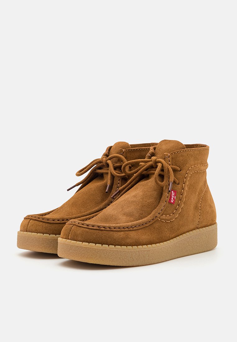 Bottes chevilles en suede taupe avec bout arrondi, couture décorative et fermeture à lacets. La semelle en caoutchouc offre une bonne traction.