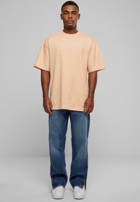 T-shirt oversize pêche à manches courtes, associé à un jean droit bleu et des baskets blanches. Look décontracté, coupe relaxée, texture lisse.