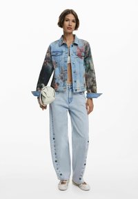 Veste en denim avec des manches à motifs floraux, jeans droit bleu clair avec des détails de boutons, et un sac blanc. Tissu texturé.