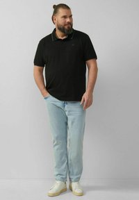 Schwarzes Poloshirt mit grünen Kragenakzenten, kombiniert mit hellblauen Jeans und weißen Sneakers. Der Schnitt ist lässig und entspannt.