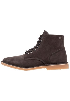 Bottine en daim brun foncé avec lacets à l'avant et semelle en caoutchouc beige clair, vue de profil sur fond blanc.