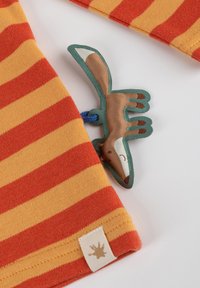 Gestreifter Baumwollstoff in Orange und Gelb, mit einem fuchsförmigen Etikett in Braun und Creme sowie einem blauen Befestigungsband.