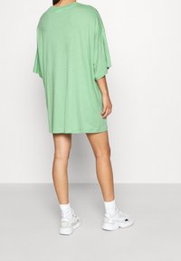 Camiseta de gran tamaño en color verde menta con mangas cortas, textura suave y escote redondeado. Combinada con zapatillas blancas y calcetines.