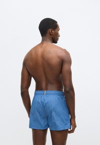 Μπλε μαγιό σορτς από ελαφρύ ύφασμα, με ελαστική μέση και μικρή λεπτομέρεια στο πίσω μέρος.