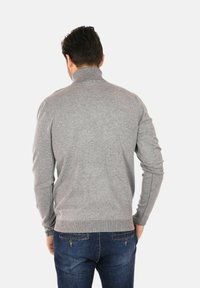 Maglione grigio con colletto alto, polsini e orlo a costine. Texture morbida, design aderente e maniche lunghe. Indossato con jeans in denim scuro.