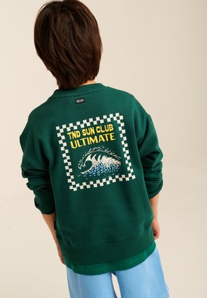 Grüner Sweatshirt mit einem Rahmen-Design im Schachbrettmuster, dem Text "TND SUN CLUB ULTIMATE" und einer Wellen-Grafik auf der Rückseite. Das Material wirkt weich.