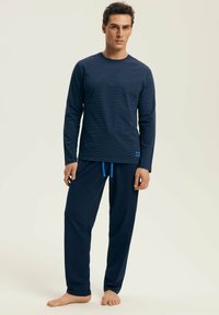 Marynarska koszula z długim rękawem w paski z niebieskimi akcentami, połączona z luźnymi, ciemnoniebieskimi spodniami z elastycznym pasem.