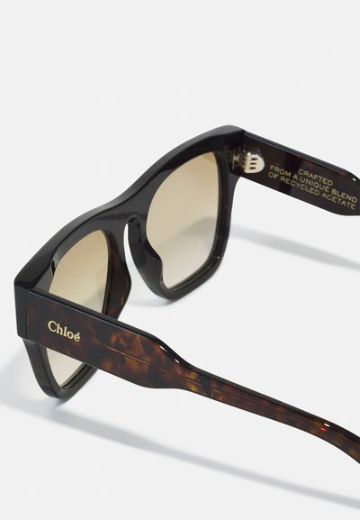 Tortoiseshell sunglasses with a chunky black and brown acetate frame. Brown gradient lenses and gold brand detail on the temple.