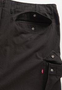 Svarte bomullsbukser med flere lommer, inkludert en lomme med trykknapp og en mindre skrå lomme, med et rødt Levi's-merke.