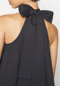 Robe noire à dos nu avec un grand nœud à l'arrière. Le tissu semble léger et lisse, avec un design simple et élégant.