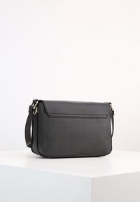 Svart lädercrossbody-väska med en strukturerad form, platt framflik, subtilt texturerad yta och justerbar rem med detaljer i guldton.