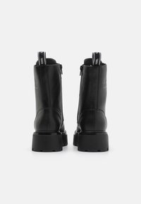 Bottines en cuir noir avec une texture lisse, semelle en caoutchouc épaisse, fermeture éclair à l'arrière, et languettes de tirage avec des accents de marque.