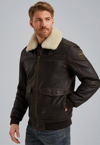 Brun læderjakke med en hvid kunstpelskrave, lynlåsåbning, to frontlommer og ribbet manchetter og kant.