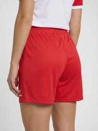 Persoon draagt rode sportshorts en een wit T-shirt met rode mouwen, van achteren getoond van taille tot halverwege de dij.
