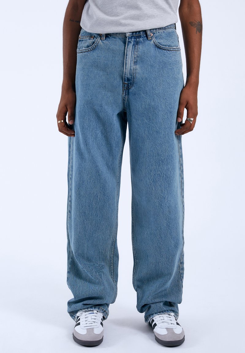 Lichtblauwe wijde jeans gemaakt van denim met een vervaagde textuur. Bevat vijf zakken, een knoopsluiting en zichtbare stikseldetails.