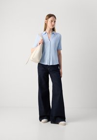 Chemise à manches courtes bleu clair avec boutons, jean large foncé et baskets blanches ; portant un sac en bandoulière de couleur crème. Design simple et épuré.