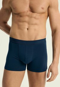 Ciemnoniebieskie bokserki w dopasowanym kroju, wykonane z gładkiego materiału. Posiadają szeroki elastyczny pas w talii oraz konturowany kształt miseczki.