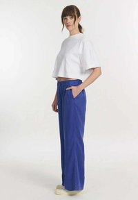 Witte cropped t-shirt met korte mouwen, gecombineerd met blauwe wijde broek met een elastische tailleband en zijzakken.