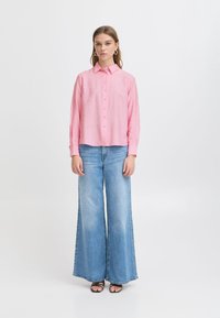 Helles rosa Hemd mit Knöpfen und Kragen, kombiniert mit weit geschnittenen, hellblauen Jeans. Das Outfit hat eine lockere Passform und ein glattes Textilgefühl.