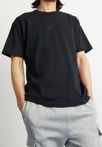 Svart bomullst-shirt med korta ärmar och rundad halsringning, med en diskret svart Nike-logotyp på bröstet. Kombination med gråa mjukisbyxor.