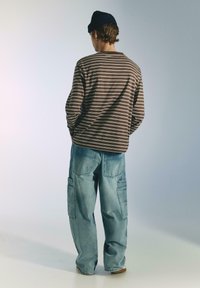 Csíkos barna hosszú ujjú ing és világoskék bő szabású cargo farmerek nagy zsebekkel. Hétköznapi kötött sapka. Texturált anyag, laza szabás.
