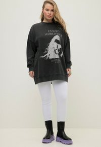 Överdimensionerad grå sweatshirt med grafiskt tryck, tillsammans med vita leggings och svarta knähöga stövlar med lila sulor. Slät tygtextur.