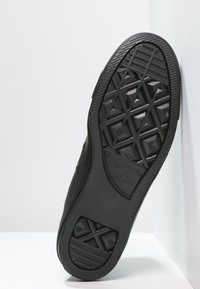 Svart gummisko med en texturerad sula som har ett geometriskt mönster och logo. Sidovy visar skons platta design.