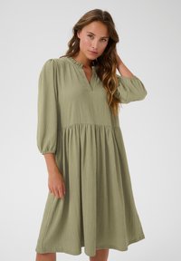 Grünes, strukturiertes Kleid mit V-Ausschnitt und Rüschensaum, dreiviertellangen Puffärmeln und einem fließenden, gestuften Rockdesign.