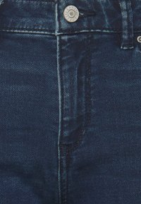 Mörkblå denimjeans har hög midja, klassisk femfickdesign, metallknäppning och synliga sömnadsdetaljer längs sömmarna.