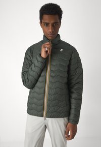 Green puffy jacket with quilted texture, high collar, and a full zipper featuring yellow and white accents. Logo on upper left side.