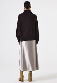 Dunkelbrauner, übergroßer Pullover mit hohem Kragen, kombiniert mit einem langen, silbernen Satinrock und beigen Blockabsatzstiefeln. Einfaches und strukturiertes Design.