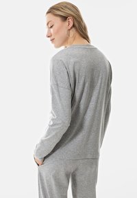 Grijze langemouwtop van zachte stof, met een relaxte pasvorm en een ronde halslijn, gecombineerd met bijpassende grijze broek. Subtiele gemêleerde textuur zichtbaar.