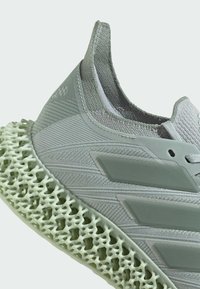Lichtgrijze sport sneaker met een bovenwerk van textuurstof, ronde neus en een onderscheidende groene, roostervormige zool.