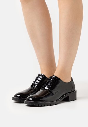 Chaussures en cuir verni noir à lacets avec un petit talon carré et une semelle en caoutchouc texturé, présentant une finition lisse et un design minimaliste.