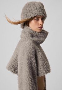 Pelerină gri din blană artificială, cu guler înalt și mâneci scurte, asortată cu o pălărie similară. Textură moale cu aspect pufos, design minimalist.