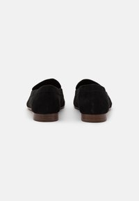 Mocassins en suede noir avec de petits talons en bois, présentant un bout arrondi et un minimum de détails de couture pour un design épuré et polyvalent.
