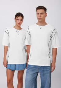 White t-shirts with short sleeves, featuring black side piping details. The fabric appears soft with a relaxed, boxy fit.