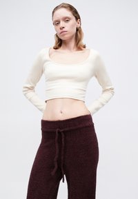 Krémový crop top s dlhým rukávom a štvorcovým výstrihom, skombinovaný s bordovými plyšovými teplákmi s šnúrkou a textúrovanou tkaninou.
