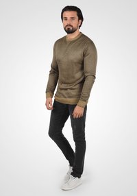 Suéter de punto de cuello redondo en marrón claro con un patrón texturizado, combinado con jeans ajustados negros y zapatillas blancas.