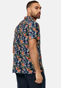 Camisa de manga corta en azul marino con un vibrante estampado floral que presenta flores rojas y amarillas, hojas verdes y un corte relajado.