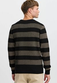 Knitted sweater featuring horizontal black and gold stripes, ribbed cuffs, and a round neckline. Texture appears woven and slightly open.