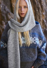 Grå striktrøje med blå og hvide geometriske mønstre, parret med et matchende gråt tørklæde. Har en blød tekstur og en hyggelig design.