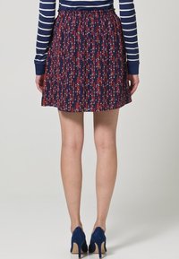 Jupe marine avec motif à pois rouge et blanc, taille élastique, design évasé, longueur au-dessus du genou, associée à des chaussures à talons hauts marines.