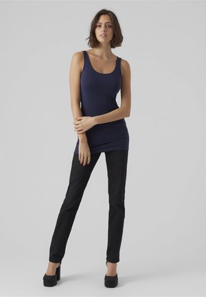 Marinblå linne med rundad halsringning, kombinerat med svarta skinny jeans och högklackade skor. Slät tygkvalitet och åtsittande design.