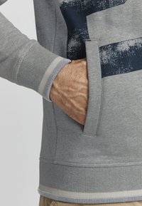 Grauer Sweatshirt mit strukturiertem Finish, ausgestattet mit einem marineblauen Streifenmuster, Rippbündchen und einer Seitentasche. Weicher Stoff mit bequemer Passform.