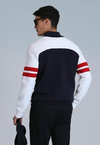 Marineblauer und weißer sportlicher Pullover mit roten Streifen an den Ärmeln, der einfarbig designt ist und einen Kragen hat. Weicher Stoff.