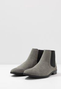 Botins cinzentos de camurça até ao tornozelo com painéis laterais elásticos, um salto baixo em bloco e um design de ponta arredondada. Textura suave com acentos minimalistas.
